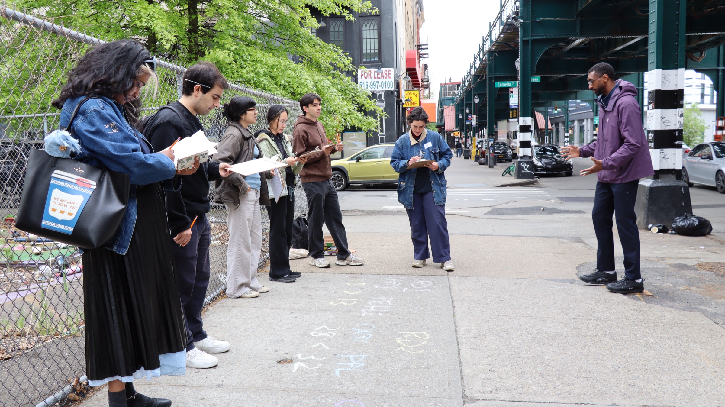 Walkers with clipboards on a Bushwick sidewalk under the elevated M train at Cornelia St, chalk math on the pavement, as the guide explains the problem