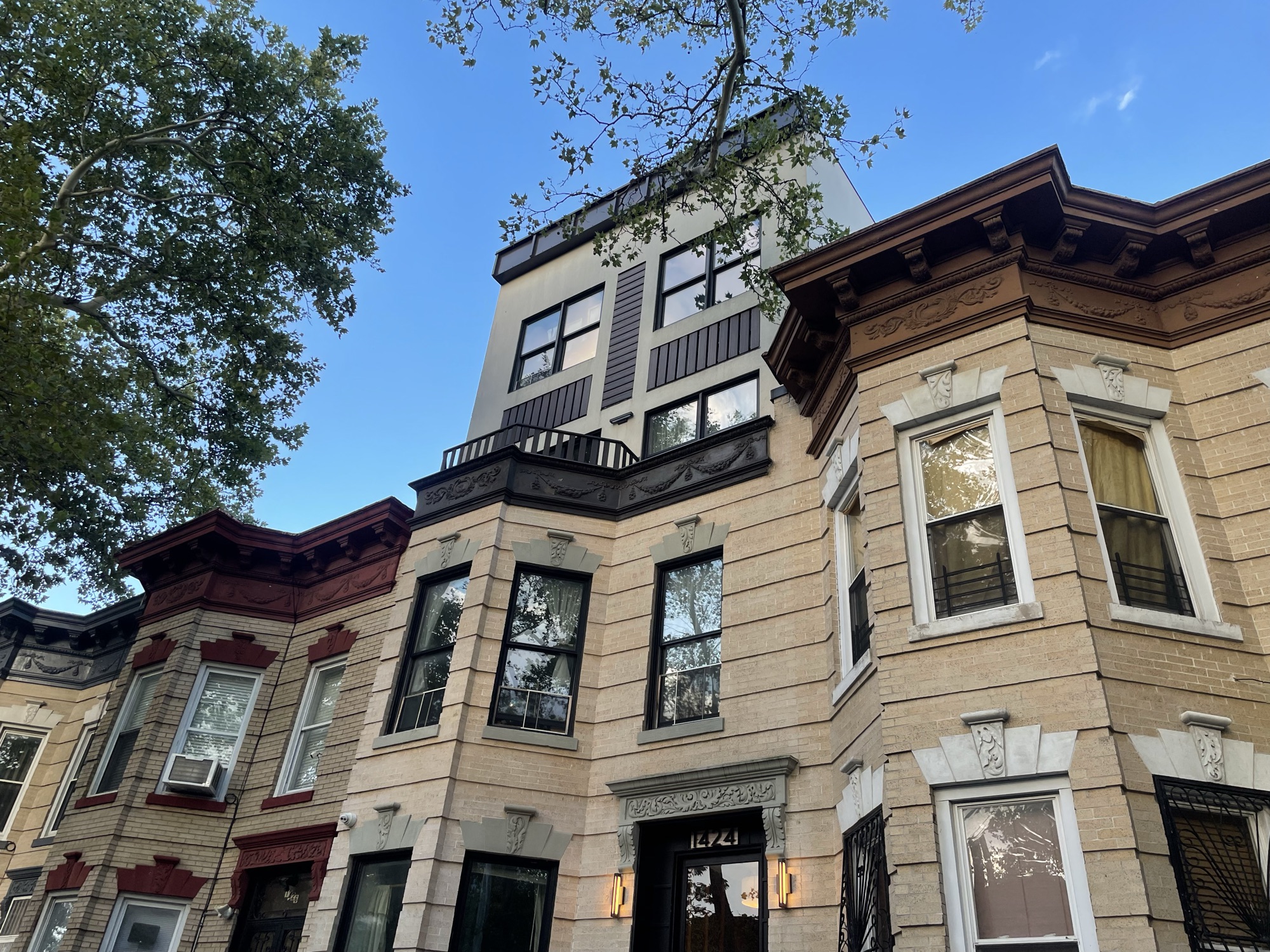 Looking up at a Bushwick rowhouse with a modern addition stacked on top, taller than its neighbors