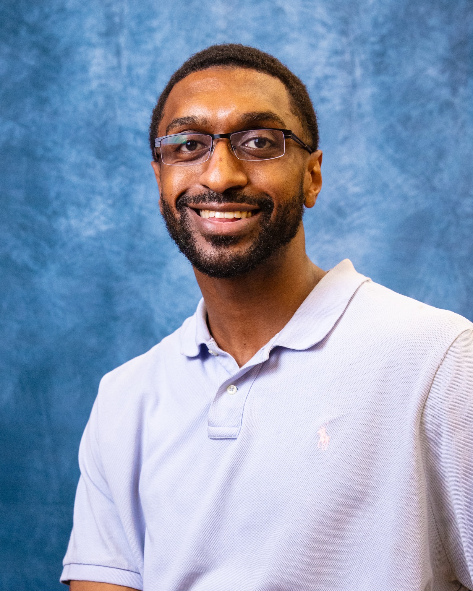 Portrait of Jordan, smiling, in glasses and a light polo