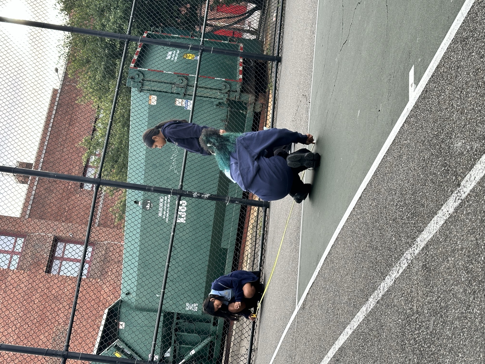 Students in school hoodies measuring the schoolyard court with a tape measure